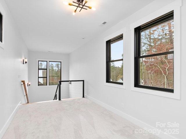 carpeted empty room with an inviting chandelier