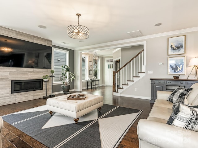 living room featuring a notable chandelier, dark hardwood / wood-style floors, crown molding, and a tile fireplace