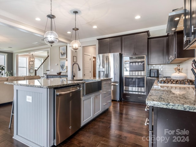 kitchen with hanging light fixtures, dark hardwood / wood-style floors, a center island with sink, and appliances with stainless steel finishes