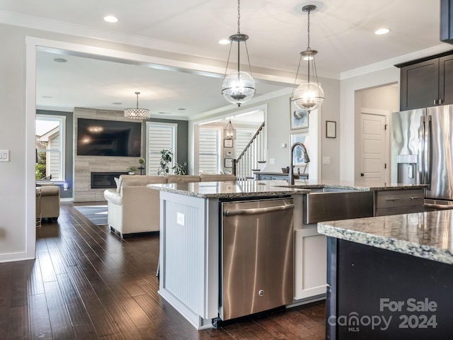 kitchen featuring dark wood-type flooring, light stone counters, a center island, appliances with stainless steel finishes, and decorative light fixtures