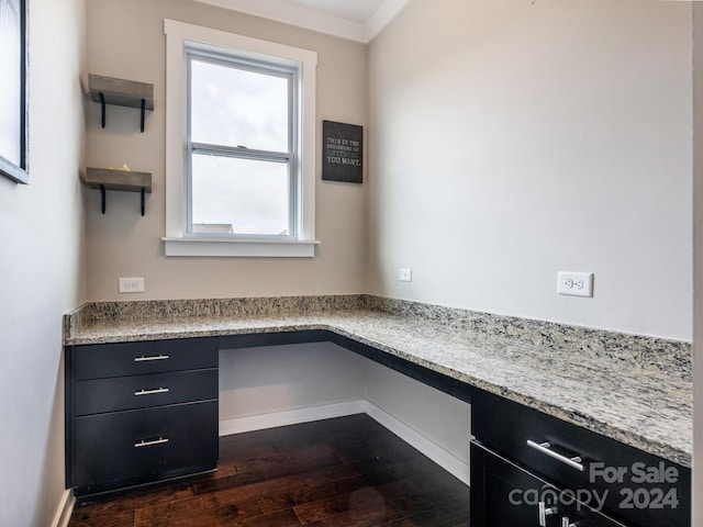 unfurnished office with dark wood-type flooring, built in desk, and crown molding