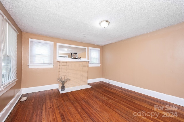 empty room with hardwood / wood-style floors, a brick fireplace, and a textured ceiling