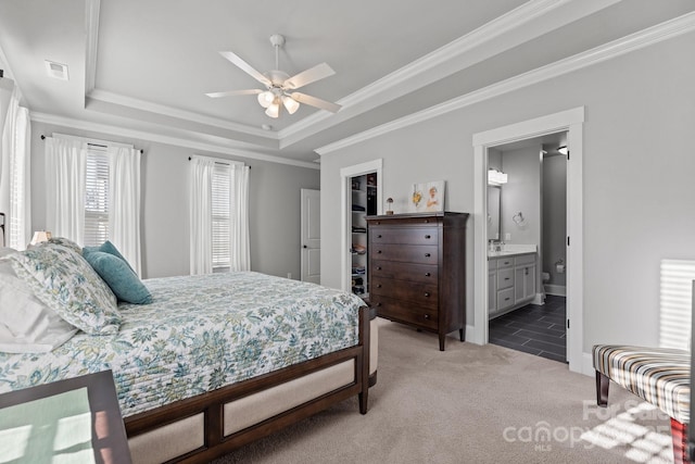 carpeted bedroom featuring ensuite bathroom, crown molding, ceiling fan, and a tray ceiling