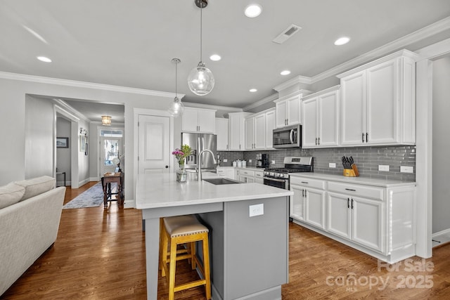 kitchen with an island with sink, sink, white cabinets, a kitchen bar, and stainless steel appliances