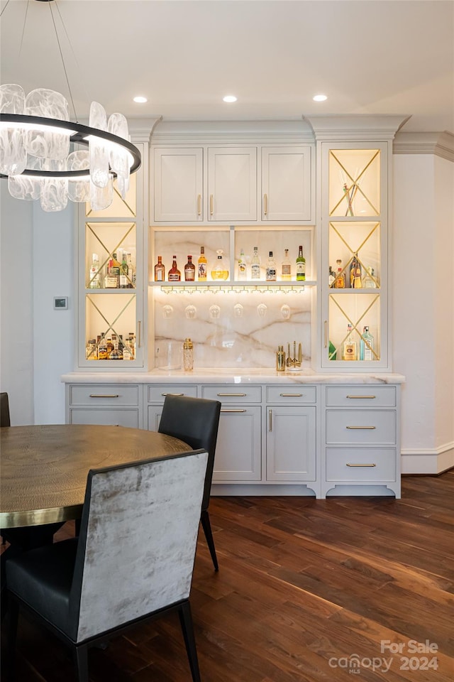 bar with dark wood-type flooring, white cabinetry, an inviting chandelier, and ornamental molding