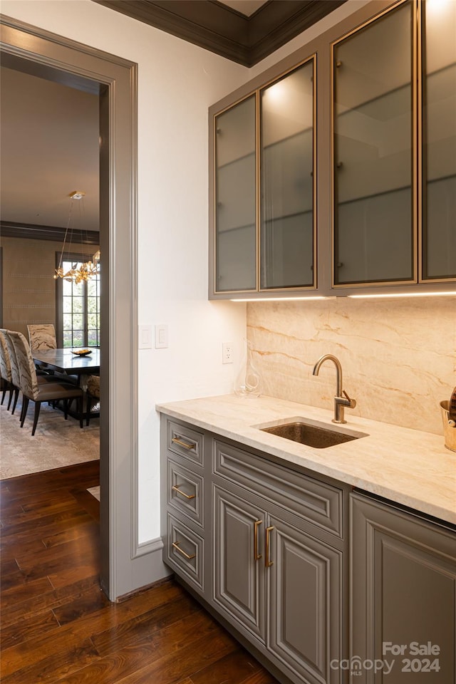 bar featuring tasteful backsplash, light stone counters, ornamental molding, sink, and dark wood-type flooring