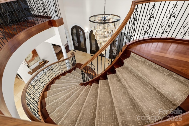 stairway with french doors, a towering ceiling, a chandelier, and tile patterned flooring