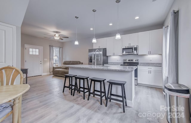 kitchen featuring stainless steel appliances, light hardwood / wood-style floors, an island with sink, white cabinetry, and decorative light fixtures