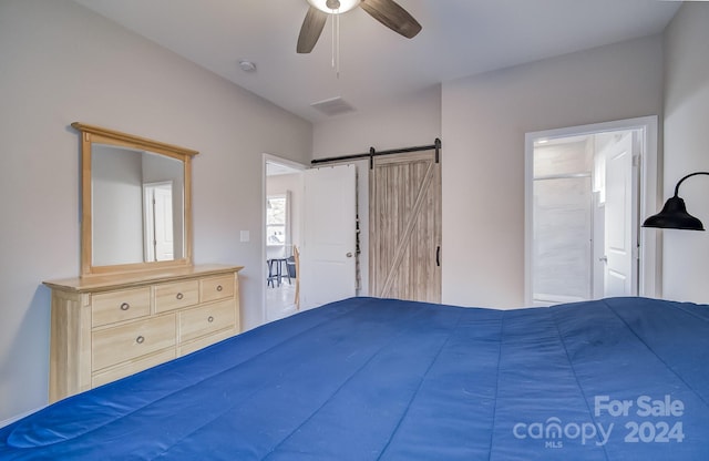 unfurnished bedroom featuring a barn door, ceiling fan, and connected bathroom