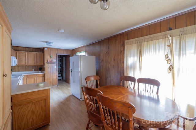 dining space with light hardwood / wood-style floors, wood walls, and a textured ceiling