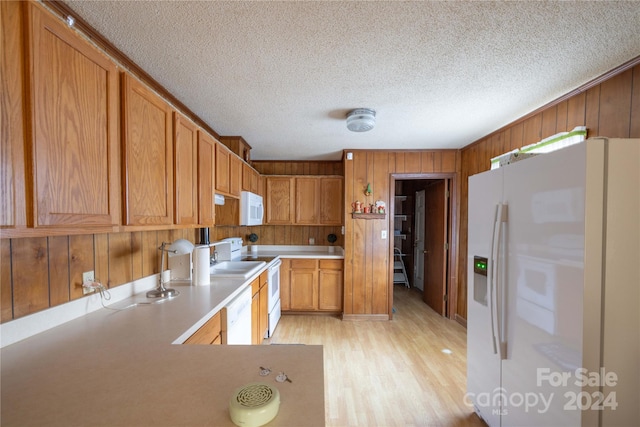 kitchen featuring white appliances, wooden walls, light hardwood / wood-style flooring, and a textured ceiling