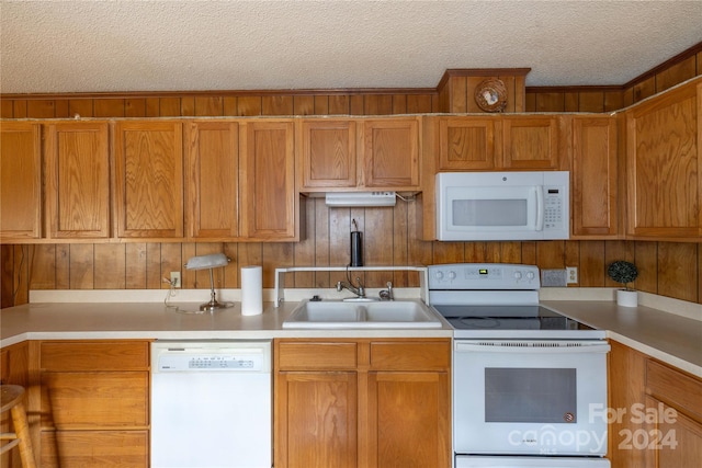 kitchen with white appliances, wooden walls, sink, and a textured ceiling