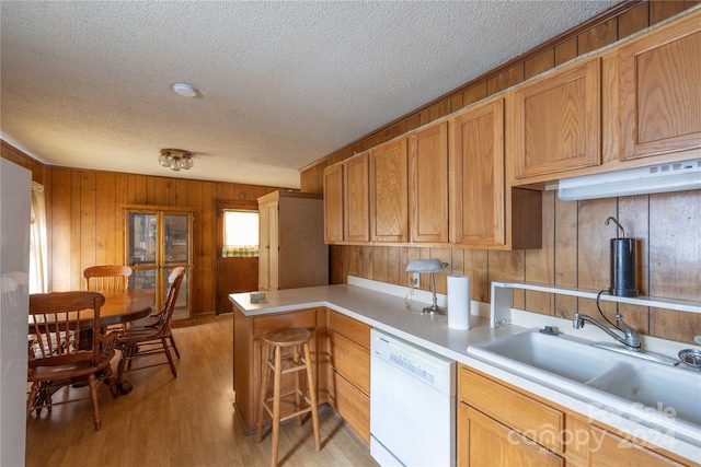 kitchen featuring light wood-type flooring, wood walls, sink, dishwasher, and kitchen peninsula