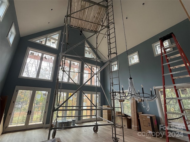 workout area featuring wood-type flooring, a towering ceiling, french doors, and a chandelier