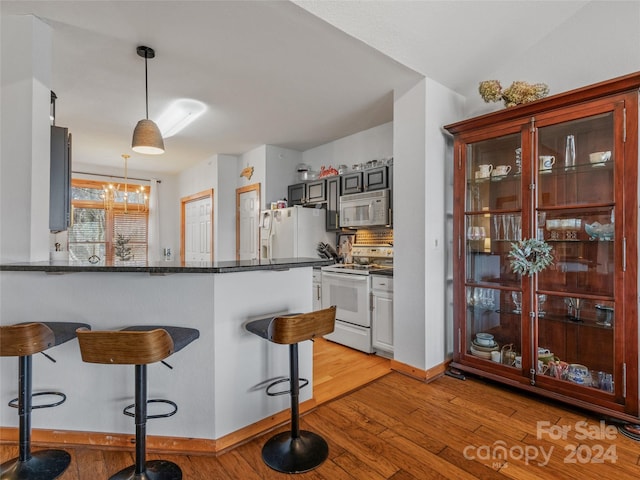 kitchen with kitchen peninsula, decorative light fixtures, white appliances, and light hardwood / wood-style floors