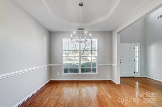 unfurnished dining area with a notable chandelier, a raised ceiling, and hardwood / wood-style flooring