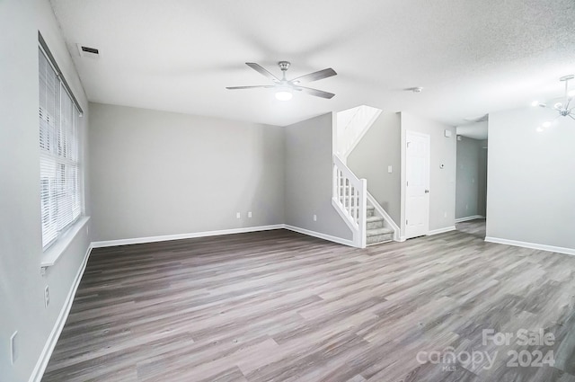 unfurnished living room with wood-type flooring, ceiling fan with notable chandelier, and a textured ceiling