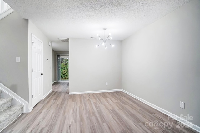 unfurnished room featuring a notable chandelier, a textured ceiling, and light hardwood / wood-style flooring