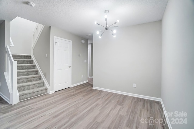 unfurnished room with light hardwood / wood-style flooring, a chandelier, and a textured ceiling