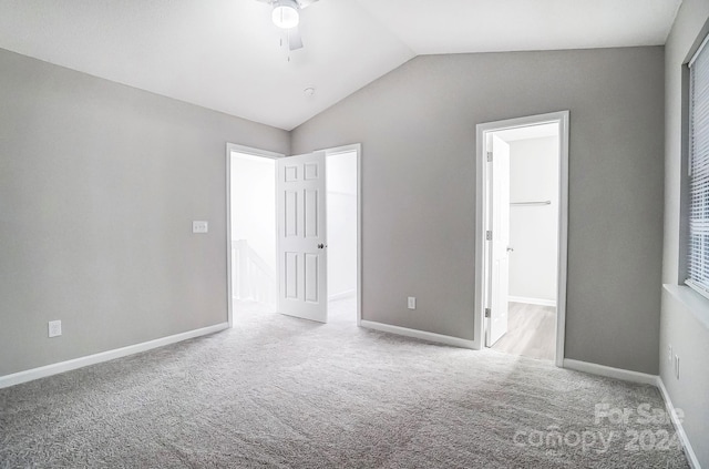 unfurnished bedroom with a spacious closet, ceiling fan, vaulted ceiling, light carpet, and a closet