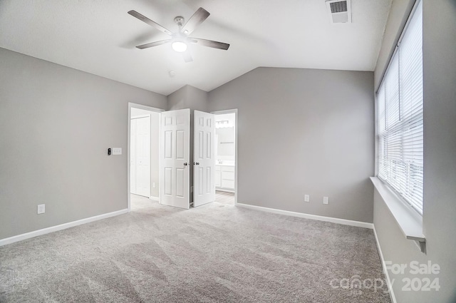 unfurnished bedroom featuring ceiling fan, light colored carpet, ensuite bath, and vaulted ceiling