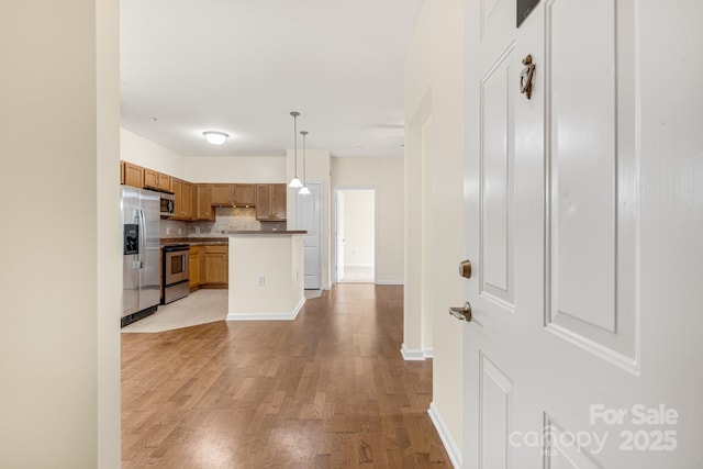 kitchen featuring pendant lighting, backsplash, light wood-type flooring, and stainless steel appliances