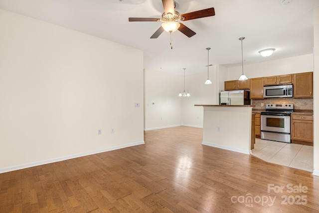 kitchen with hanging light fixtures, light hardwood / wood-style flooring, decorative backsplash, ceiling fan, and stainless steel appliances