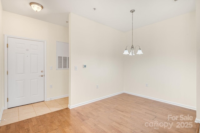 empty room with light wood-type flooring and a notable chandelier