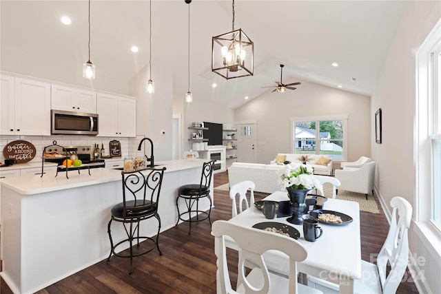 dining space with ceiling fan with notable chandelier, dark hardwood / wood-style flooring, sink, and high vaulted ceiling