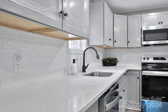 kitchen with sink, decorative backsplash, light stone countertops, appliances with stainless steel finishes, and white cabinetry