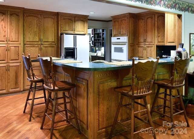 kitchen featuring crown molding, a breakfast bar, white appliances, and light wood-type flooring