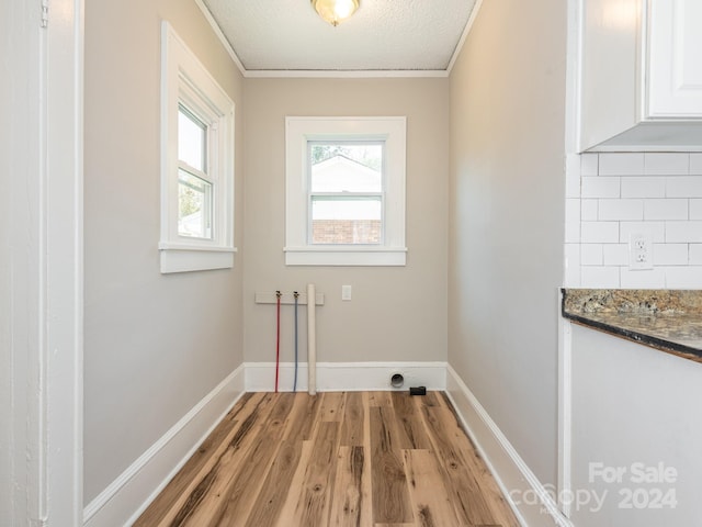 laundry room featuring a textured ceiling, light wood-type flooring, and ornamental molding