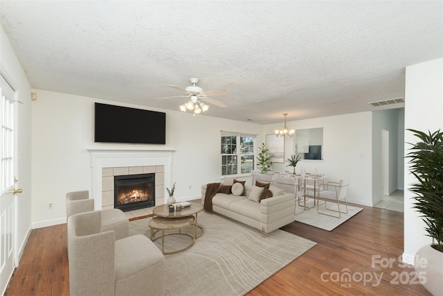 living room featuring a tiled fireplace, ceiling fan with notable chandelier, dark hardwood / wood-style floors, and a textured ceiling