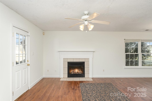 unfurnished living room featuring a tiled fireplace, ceiling fan, hardwood / wood-style flooring, and a textured ceiling