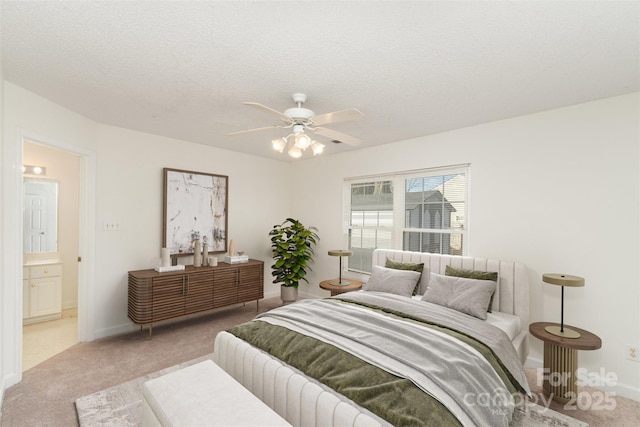 bedroom with ceiling fan, connected bathroom, light colored carpet, and a textured ceiling