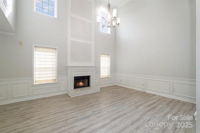 unfurnished living room with crown molding, light hardwood / wood-style floors, a brick fireplace, and a notable chandelier