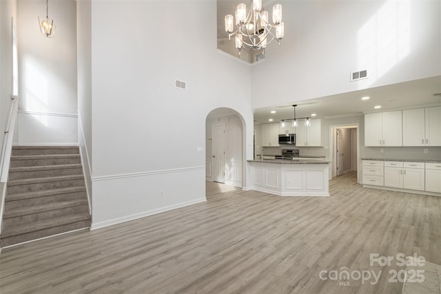 unfurnished living room with a notable chandelier, light hardwood / wood-style flooring, and a high ceiling