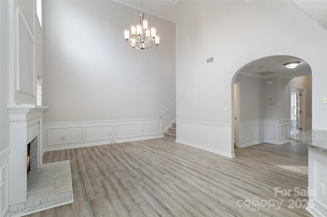 interior space featuring a brick fireplace, a notable chandelier, ornamental molding, and light hardwood / wood-style floors