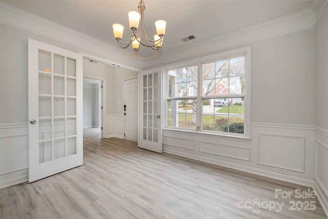 unfurnished dining area featuring an inviting chandelier, ornamental molding, light hardwood / wood-style floors, and french doors