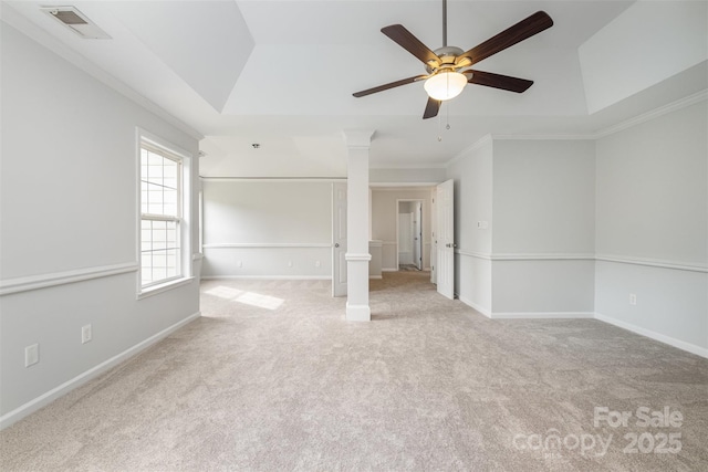 empty room featuring ceiling fan, decorative columns, ornamental molding, light colored carpet, and a raised ceiling