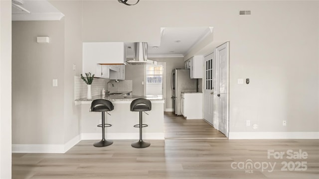 kitchen with white cabinetry, sink, a kitchen bar, exhaust hood, and kitchen peninsula