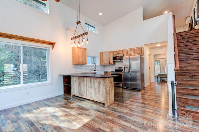 kitchen featuring a kitchen bar, stainless steel appliances, hanging light fixtures, and a high ceiling