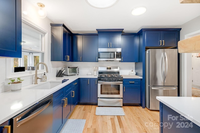 kitchen with light wood-type flooring, appliances with stainless steel finishes, sink, and blue cabinets