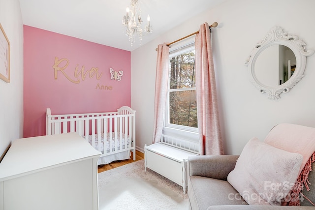 bedroom featuring light wood-type flooring, a nursery area, and an inviting chandelier