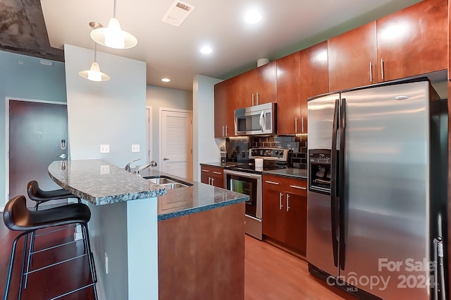 kitchen with a kitchen bar, light hardwood / wood-style flooring, hanging light fixtures, sink, and appliances with stainless steel finishes