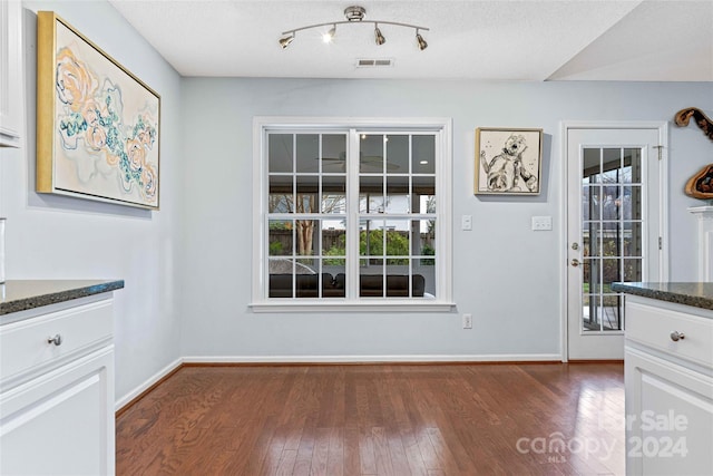 unfurnished dining area with a textured ceiling, a wealth of natural light, and dark wood-type flooring