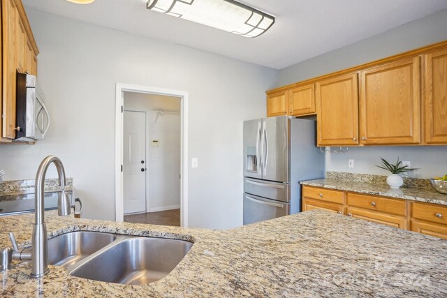 kitchen with stainless steel refrigerator with ice dispenser, sink, and light stone counters