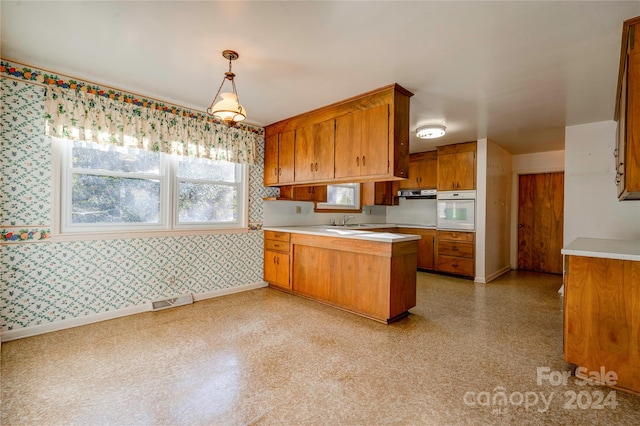 kitchen featuring kitchen peninsula, white oven, extractor fan, sink, and hanging light fixtures