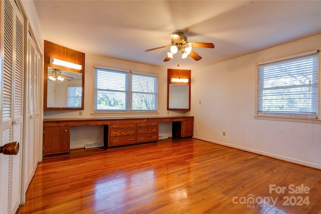 unfurnished bedroom with built in desk, hardwood / wood-style flooring, and ceiling fan