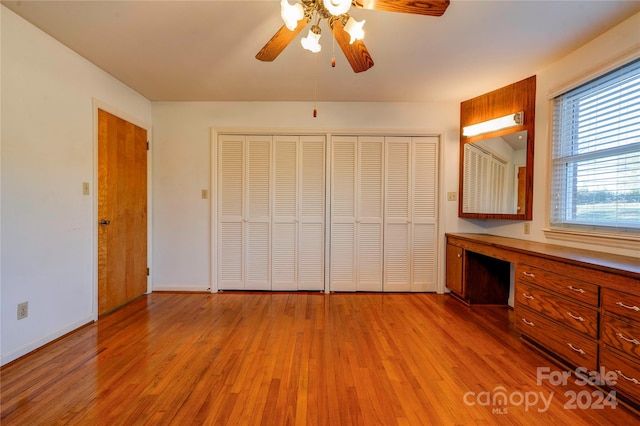 unfurnished bedroom with built in desk, light hardwood / wood-style floors, and ceiling fan